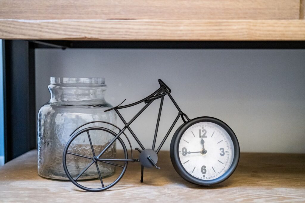 A vintage bicycle-shaped clock next to a glass jar on a wooden shelf, adding retro charm to home decor.